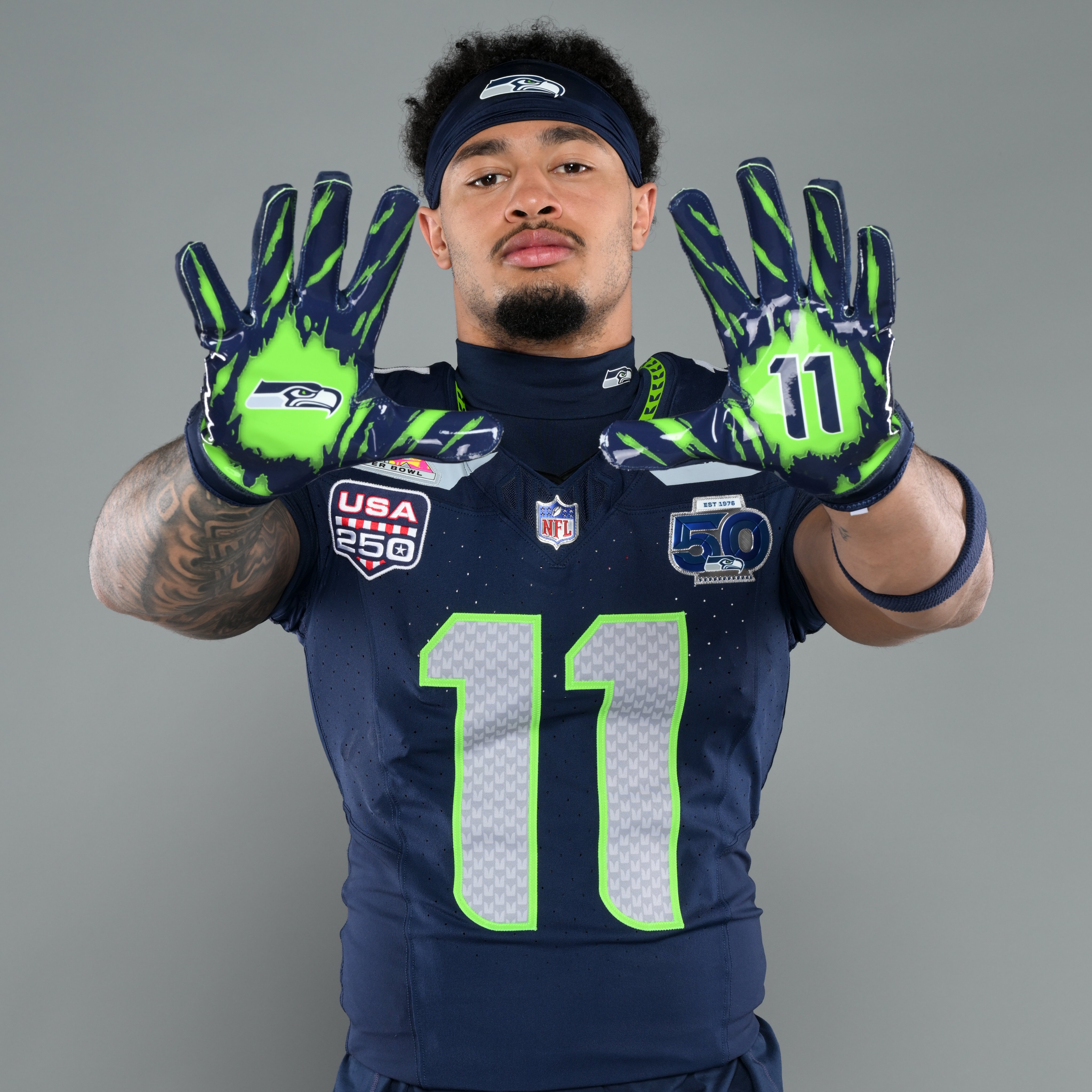 Seattle Seahawks wide receiver Jaxon Smith-Njigba wearing the navy blue Seahawks home jersey for the 2025-26 NFL season showing the USA 250 patch sewn on the right chest of the jersey directly above the NFL shield logo, the same USA 250 shield design that the NBA is now using on 2026 NBA Finals jerseys, with the Seahawks 50th anniversary commemorative patch on the opposite chest