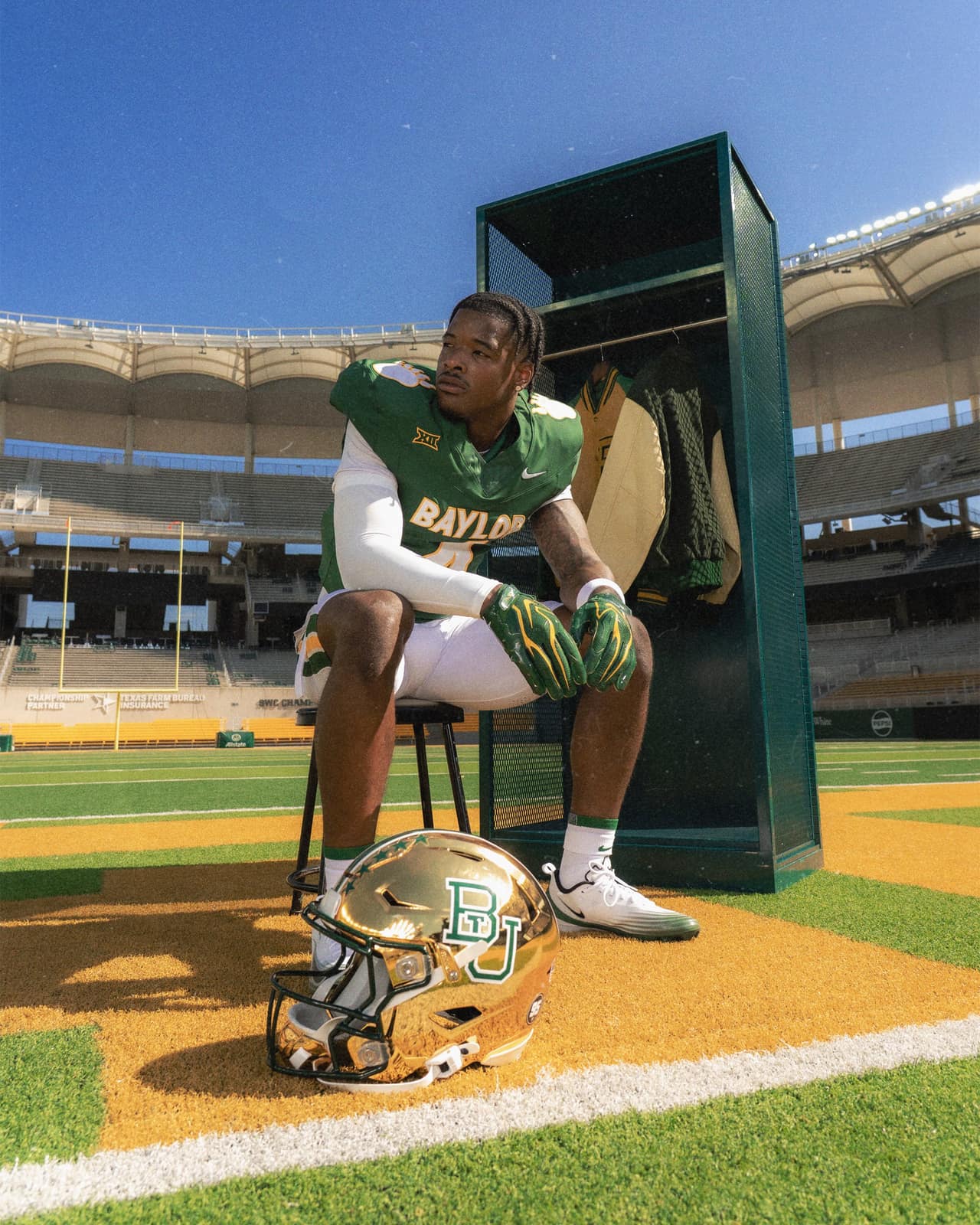 Baylor player in the 2026 green throwback jersey and white pants seated beside a green locker at McLane Stadium with the gold chrome helmet on the turf