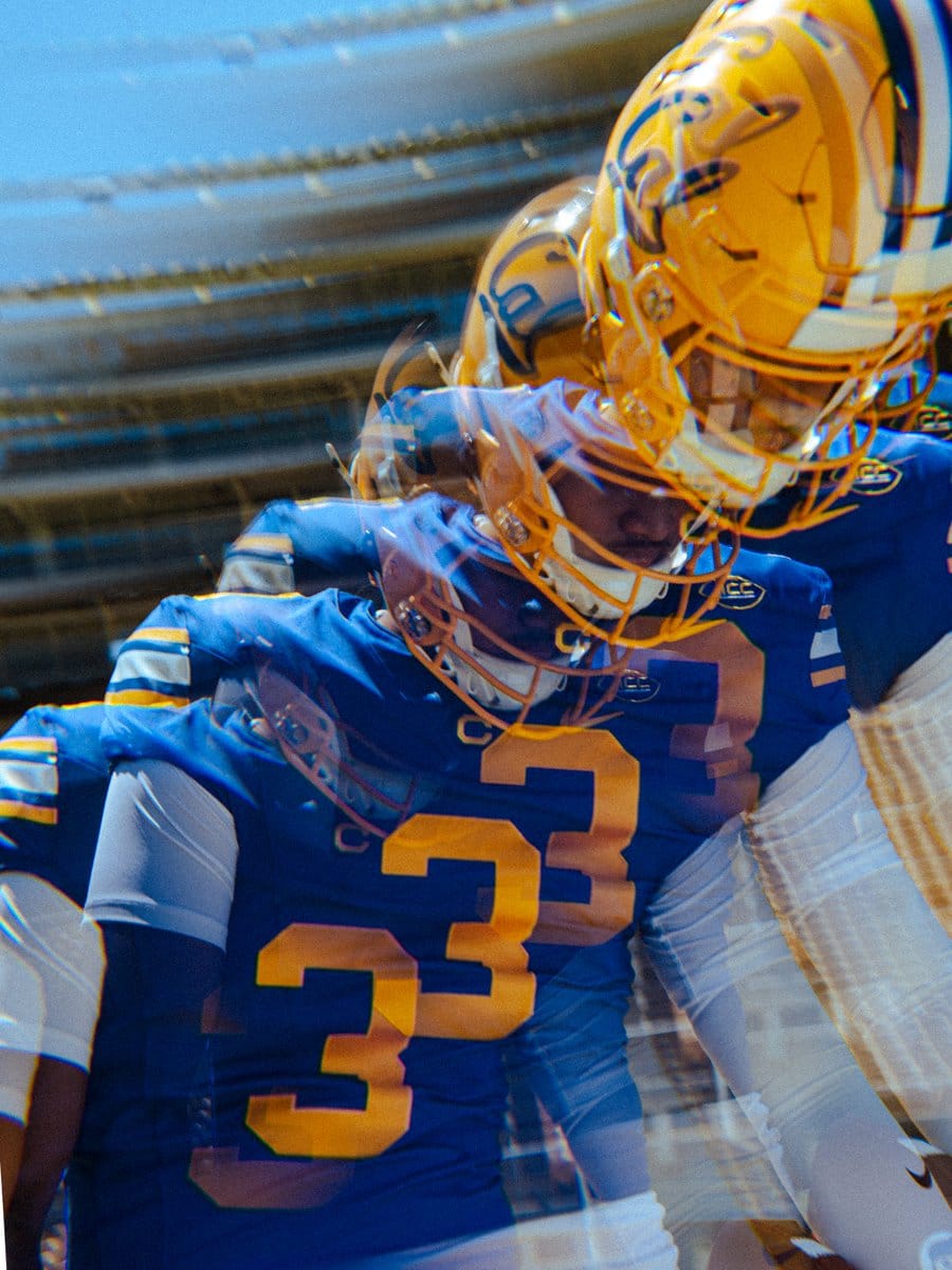 Cal Golden Bears players in the 2026 Joe Roth throwback uniforms, gold helmets and royal blue jerseys with gold numbers, shot with motion blur in the tunnel