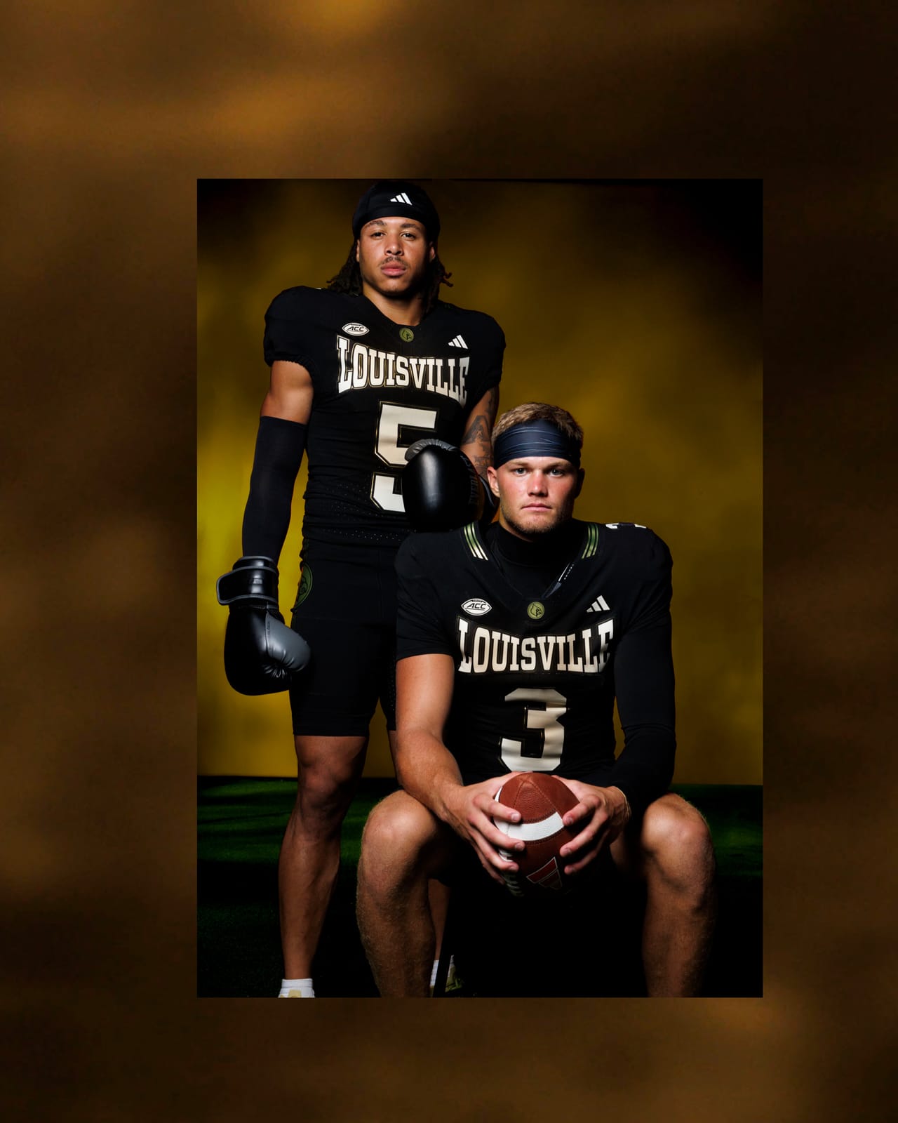 Two Louisville players in the 2026 black alternate uniform, with LOUISVILLE arched across the chest in white with gold trim and gold Cardinal logos on the pants