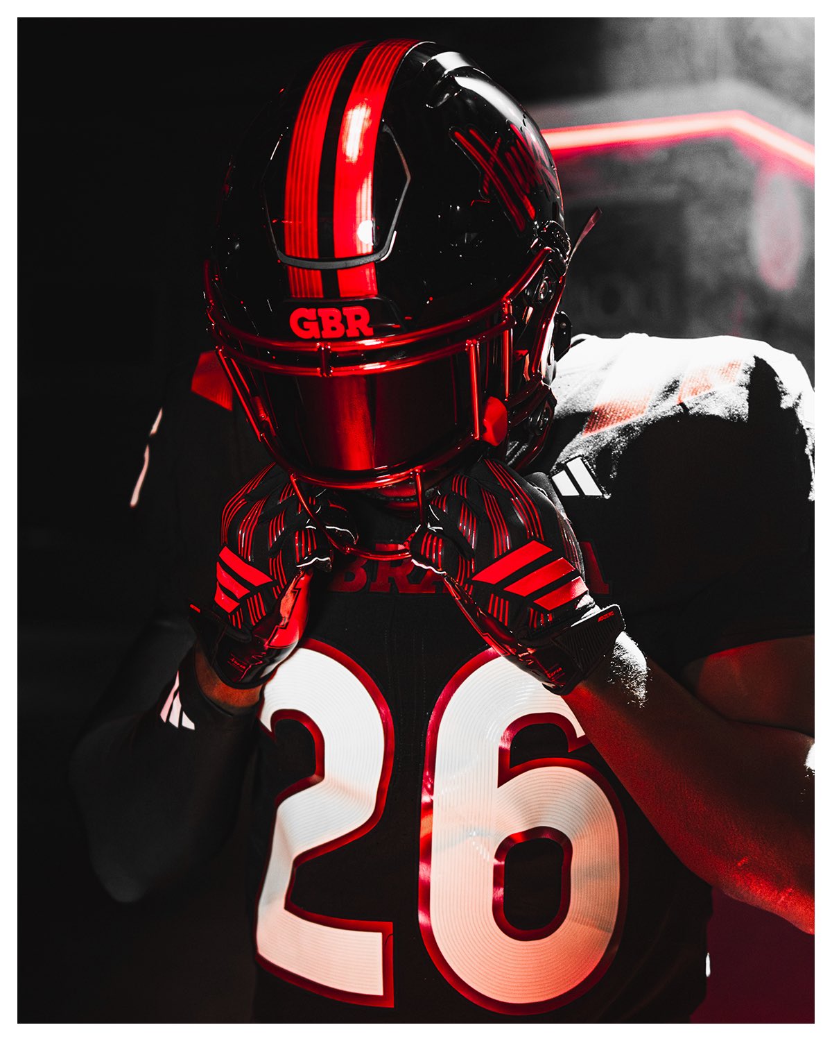 Close-up of the Nebraska 2026 blackout helmet, gloss black with a metallic red stripe and a red facemask, with GBR on the front bumper