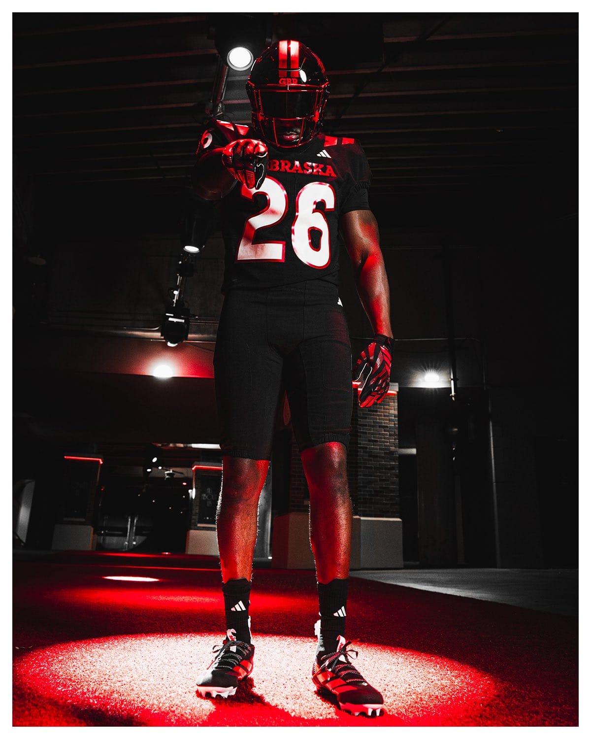 Nebraska Cornhuskers 2026 blackout uniform, a black jersey with NEBRASKA in red across the chest and large white numbers, worn with a black helmet and red facemask