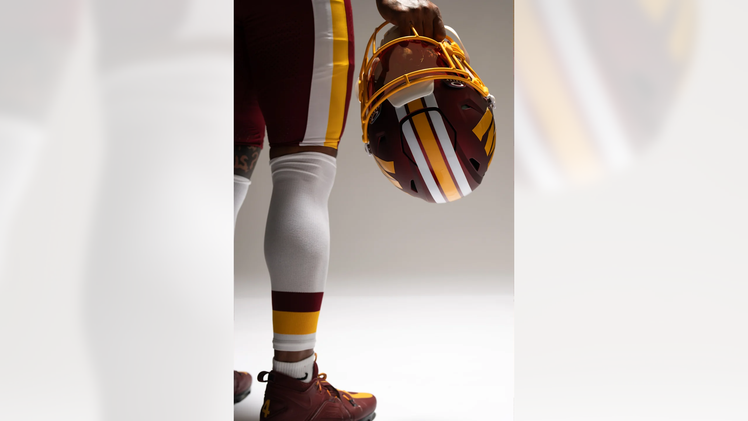 Washington Commanders player holding burgundy helmet at waist showing pants striping