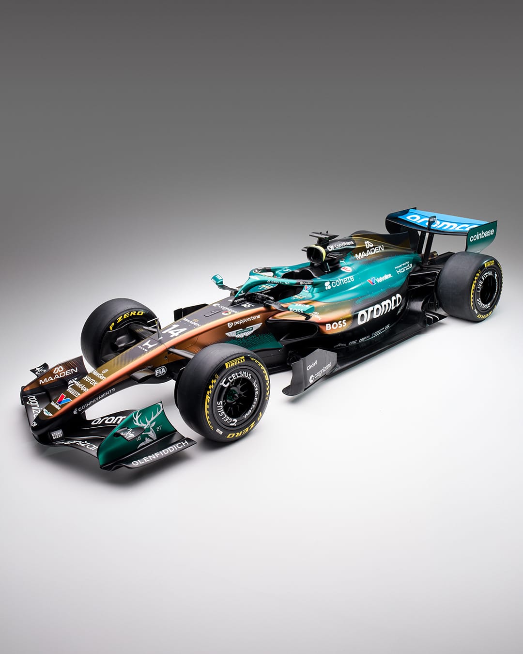 Aston Martin AMR25 F1 Monaco Grand Prix 2026 special Maaden iridescent livery side three-quarter studio shot showing the color-changing green-to-gold hexagonal mesh gradient pattern across the nose and sidepods with the MAADEN wordmark on the engine cover, the Aramco wordmark prominent on the sidepod, and Glenfiddich stag deer logo on the front wing endplate
