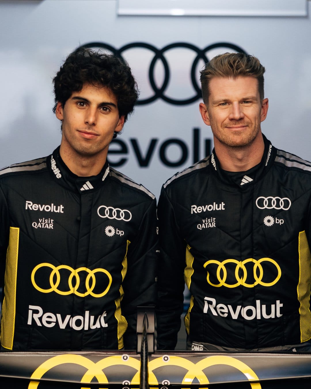 Closer head-and-shoulders portrait of Audi F1 drivers Nico Hülkenberg and Gabriel Bortoleto in the 2026 Monaco GP Tazio Nuvolari tribute black-and-yellow race suits showing the German and Brazilian flag badges below the yellow chest mark