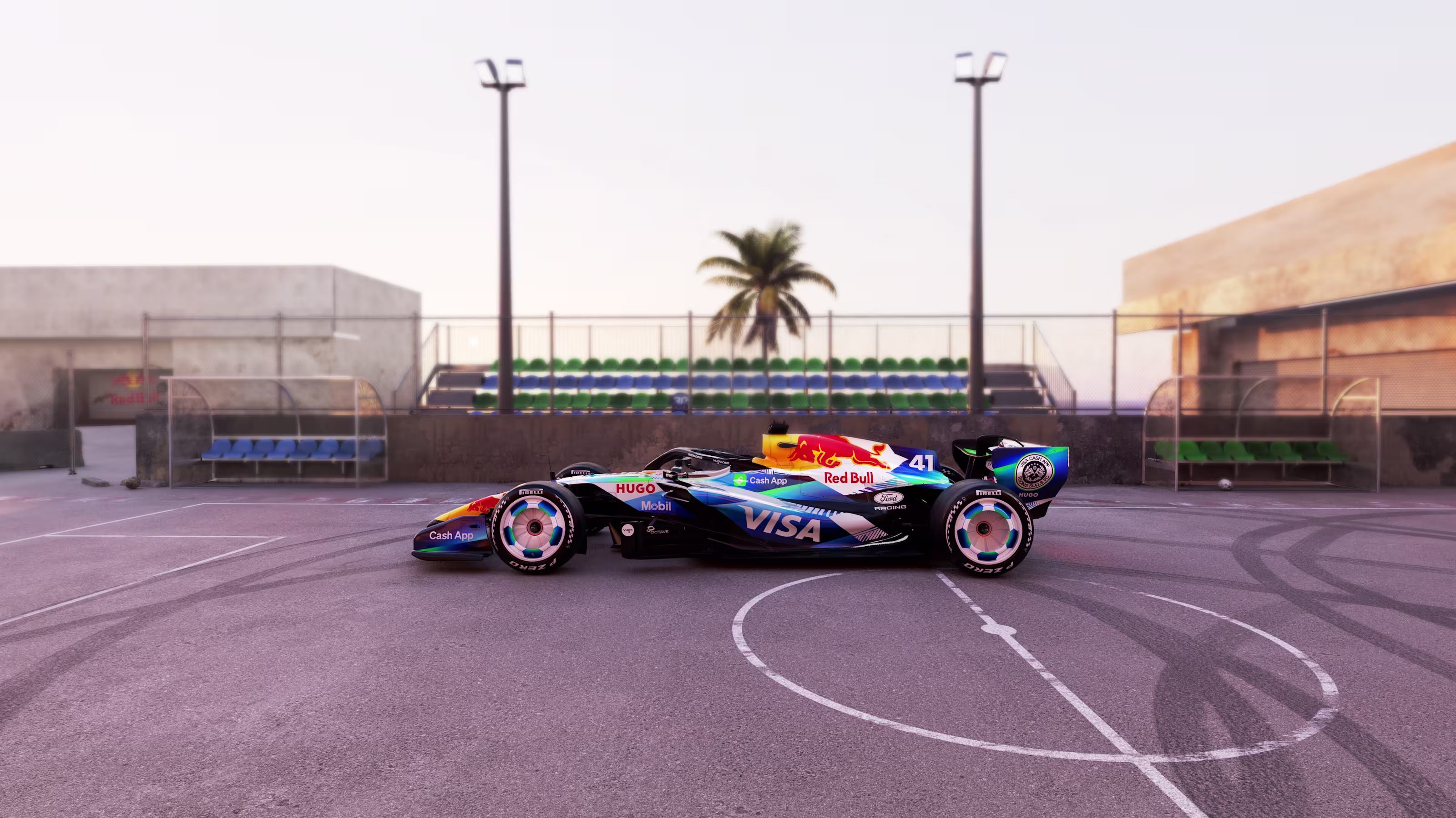 Visa Cash App Racing Bulls F1 Barcelona Grand Prix 2026 special soccer football livery full side profile of the number 41 car on a street futsal court showing the white-and-black soccer ball wheel covers on both axles, the white upper bodywork flowing into deep navy along the floor, the blue-to-teal gradient brushwork on the engine cover, the white VISA wordmark on the sidepod, and the Red Bull crest on the nose with a palm tree and bleachers behind the court fence
