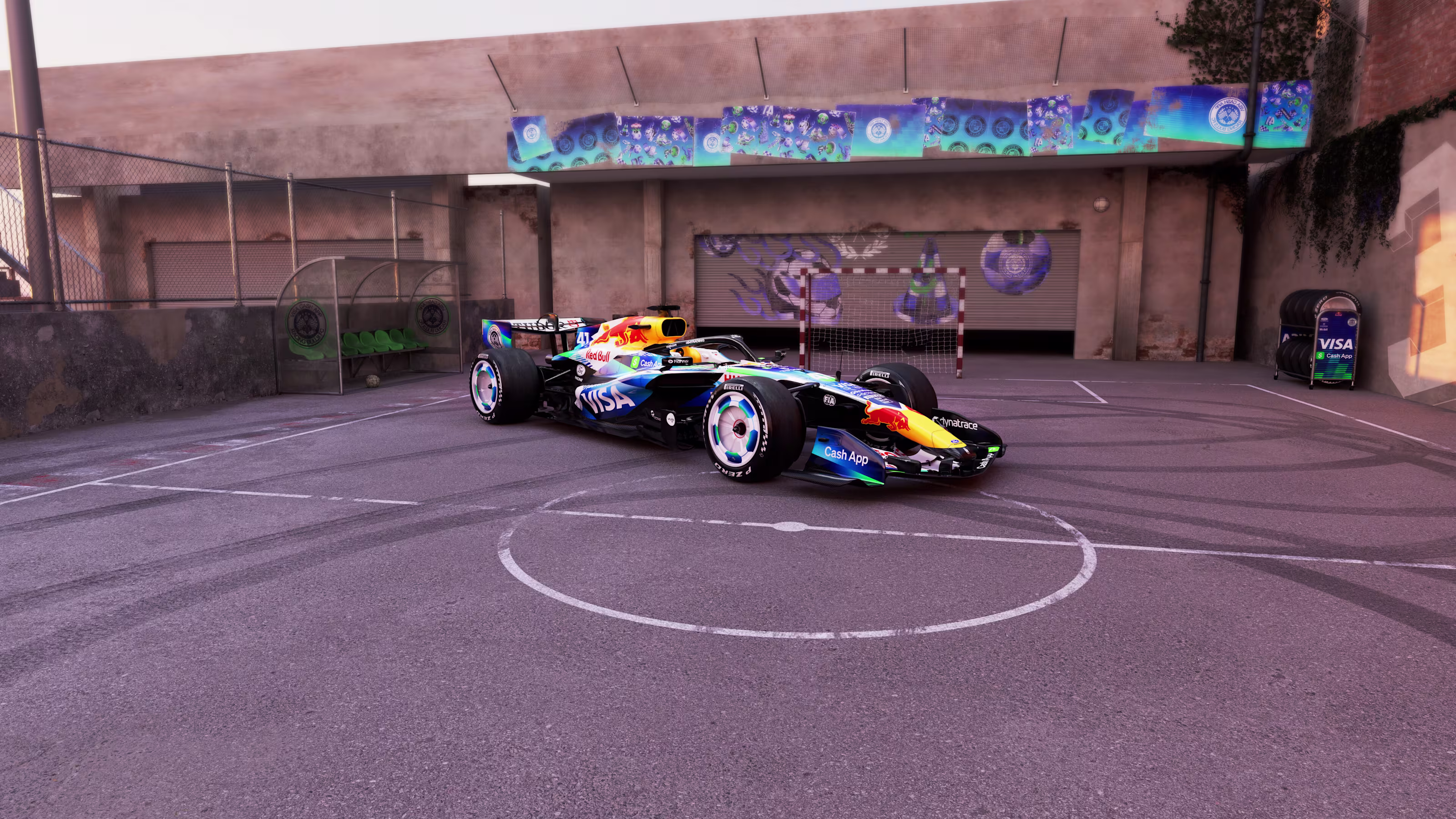 Visa Cash App Racing Bulls F1 Barcelona Grand Prix 2026 soccer football livery wide shot of the number 41 car parked in front of the futsal goal frame with a winged soccer ball mural on the garage door behind it and a Visa Cash App branded tire rack standing in the corner of the court