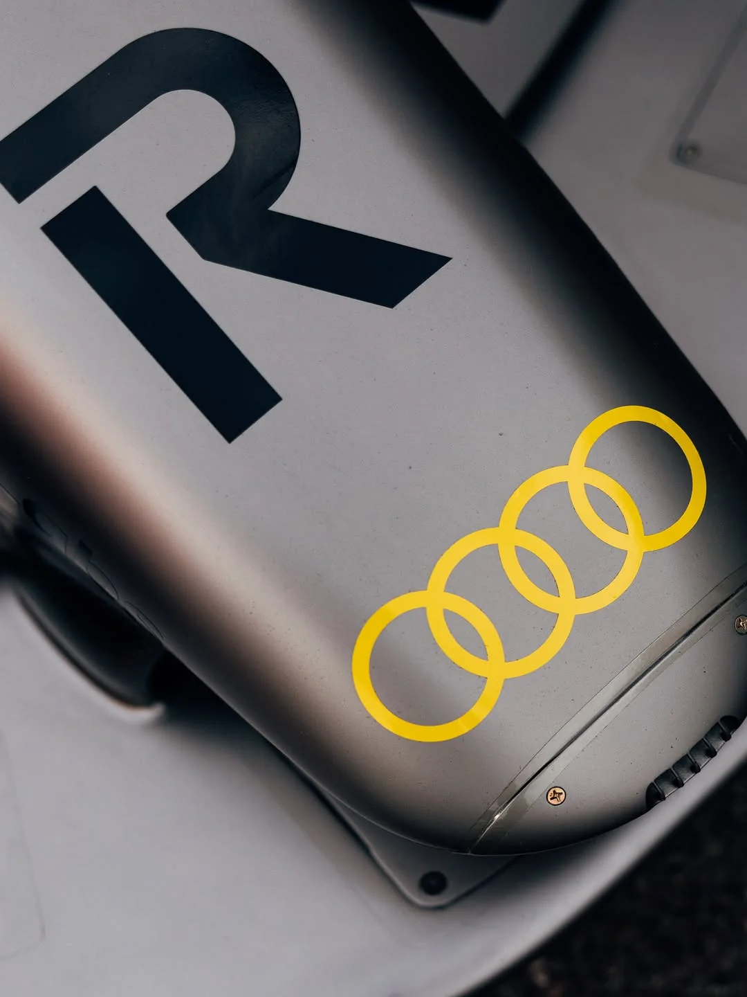 Audi F1 2026 Monaco Grand Prix Tazio Nuvolari tribute livery macro detail showing the bright Nuvolari yellow Audi four-ring lock-up on the titanium-silver carbon fiber body next to the Revolut R wordmark