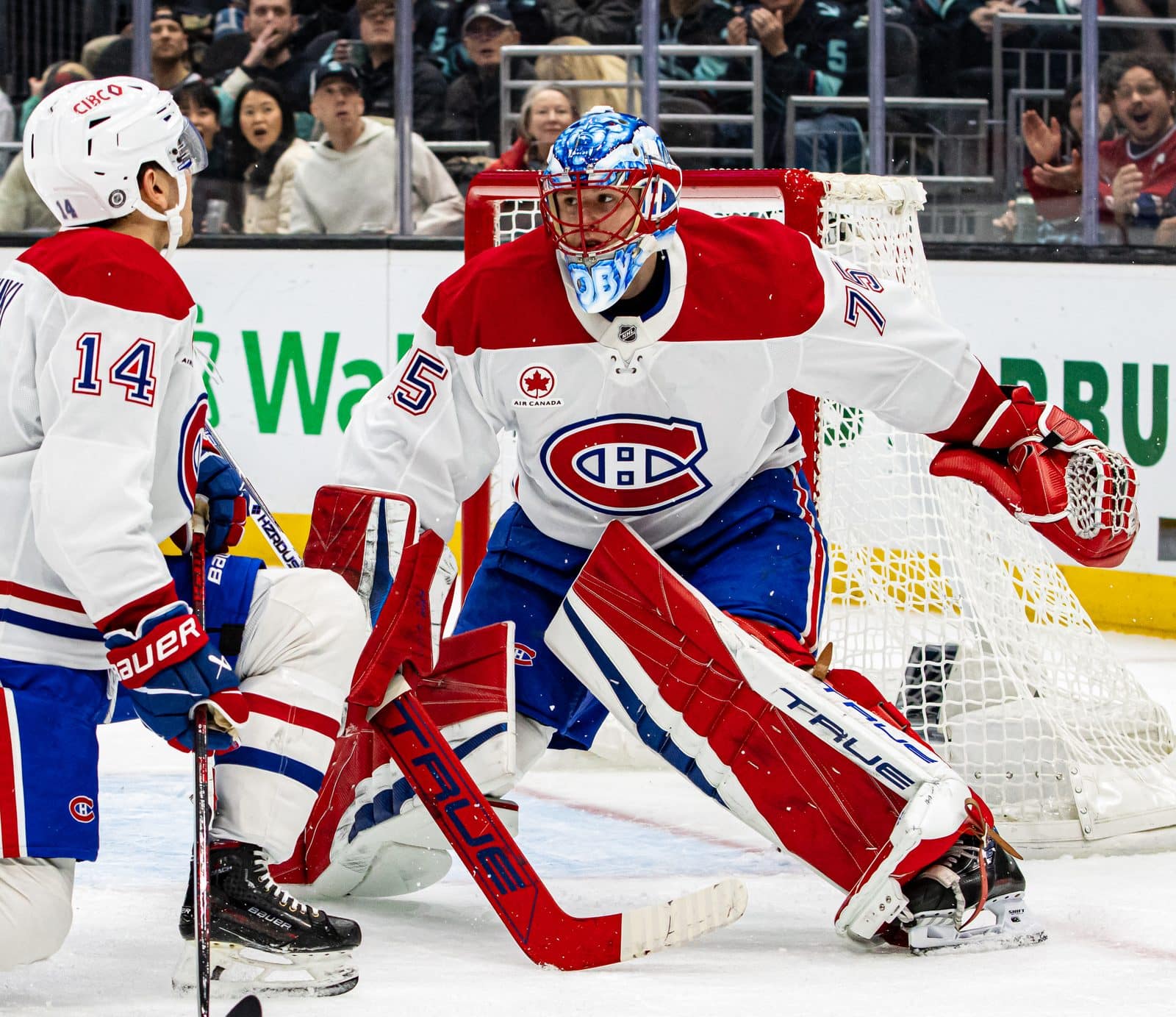 Canadiens goalie Jakub Dobeš in the white road sweater with the red, white and blue CH crest on the chest, with Nick Suzuki beside the crease, at Climate Pledge Arena in Seattle, March 12, 2025