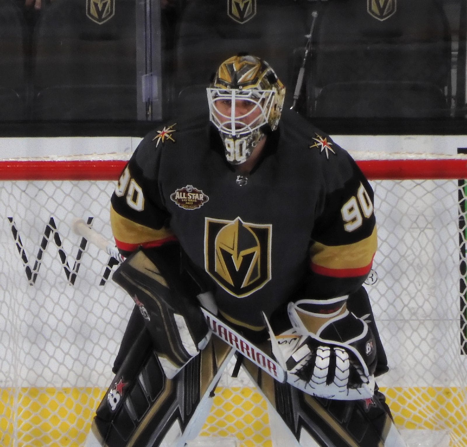 Golden Knights goalie Robin Lehner in the black sweater with the gold-and-black knight's helmet crest on the chest, in net with more helmet logos on the boards behind him, January 6, 2022
