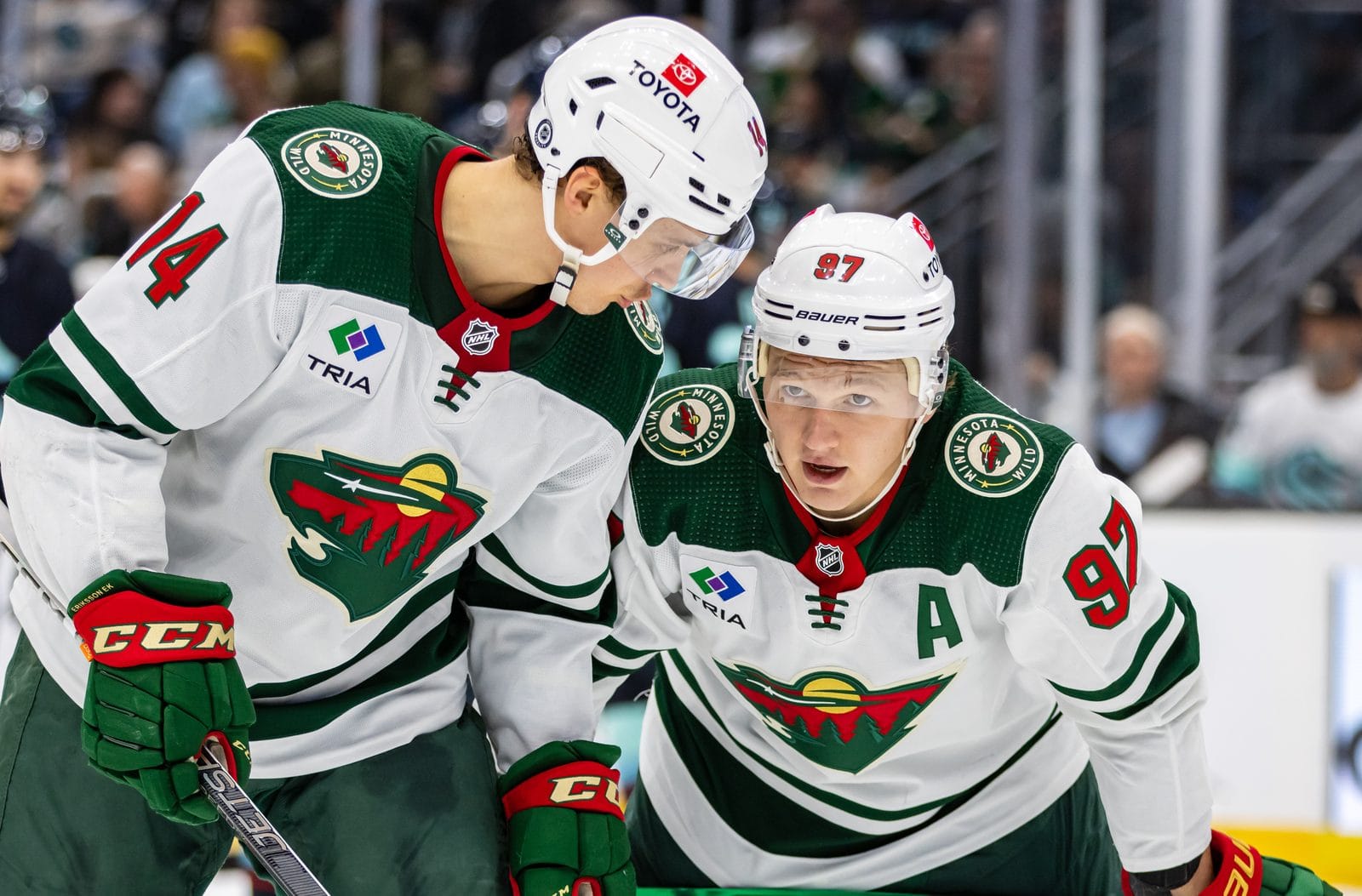 Joel Eriksson Ek and Kirill Kaprizov in the Wild's white road sweaters with the forest-and-animal-head crest on the chest and round Minnesota Wild patches on the shoulders, at Climate Pledge Arena in Seattle, December 10, 2023