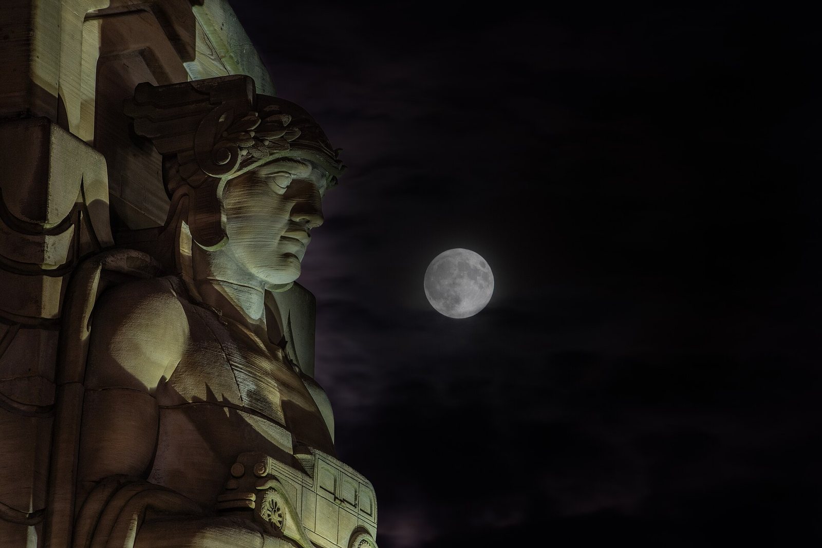 One of the Guardians of Traffic stone statues on the Hope Memorial Bridge in Cleveland, lit at night with the full moon behind it, in September 2024