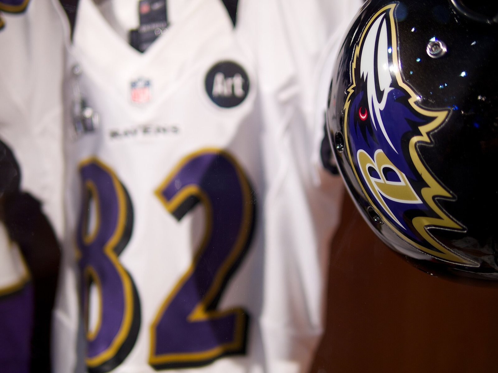 A Baltimore Ravens helmet with the purple raven head logo, with a gold B for Baltimore on the side of the head, next to a white No. 82 jersey