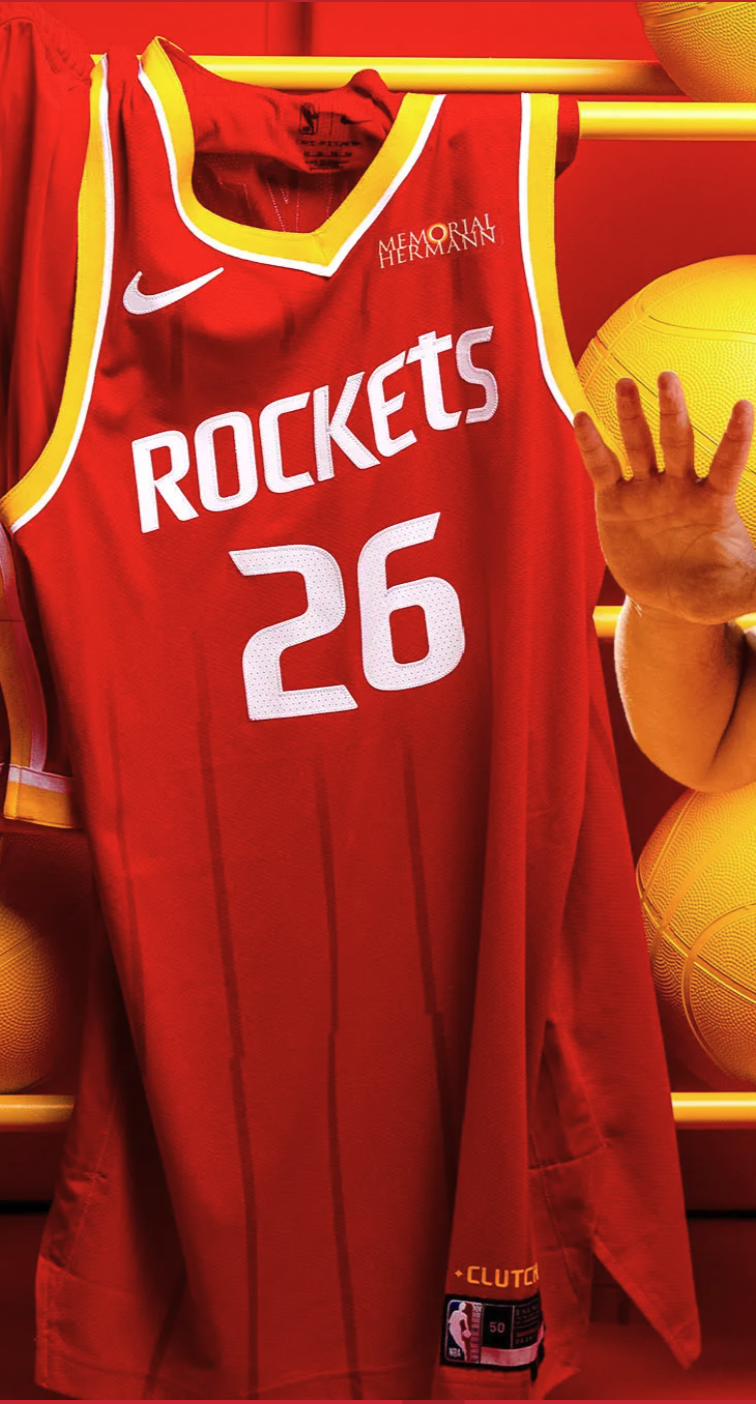 Houston Rockets 2026-27 new Icon Edition red jersey number 26 product shot on hanger with white ROCKETS wordmark, Championship Yellow drop trim, Roll Stripes side stripe, Memorial Hermann sponsor patch, and Clutch City Forever jock tag visible