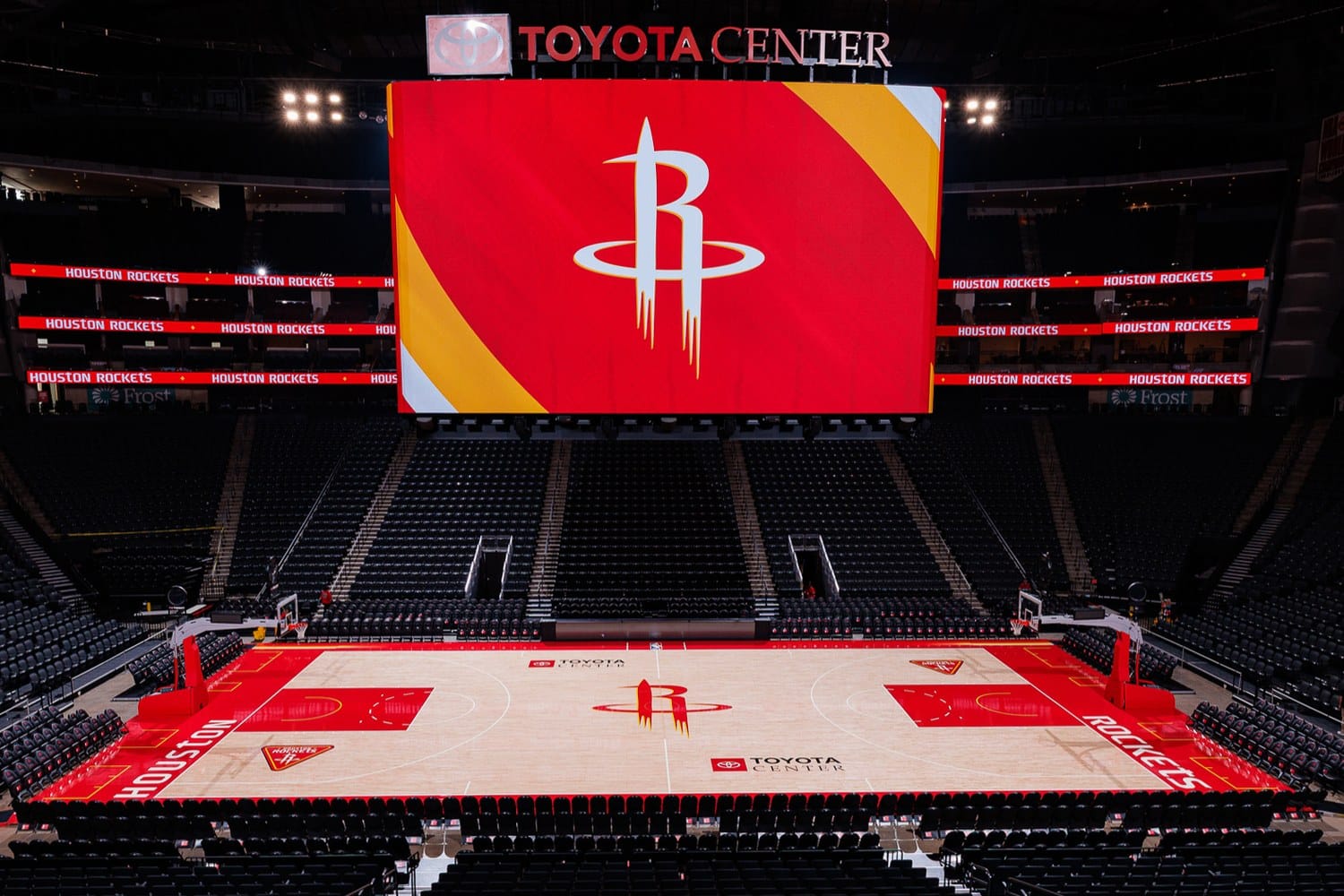 Houston Rockets Core Court at Toyota Center for 2026-27, light hardwood with a large red rocket R logo outlined in yellow at center, red painted lanes and red baselines with yellow accents