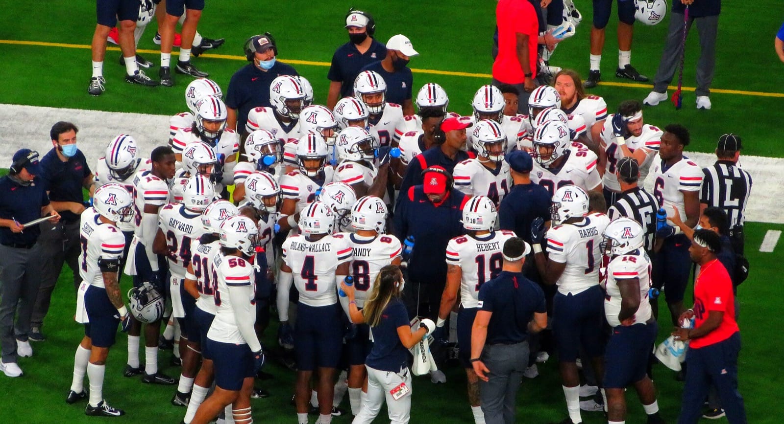 Arizona players in white jerseys and white helmets huddle on the sideline at the 2021 Vegas Kickoff Classic