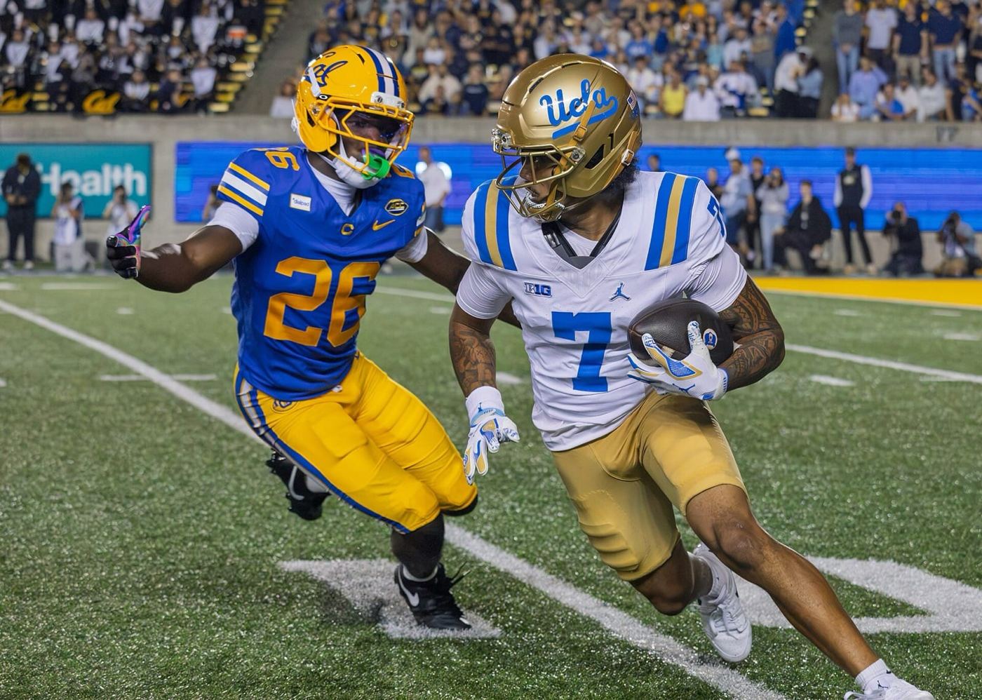 A Cal defender in a blue jersey, gold pants and gold helmet chases a UCLA ball carrier at Memorial Stadium