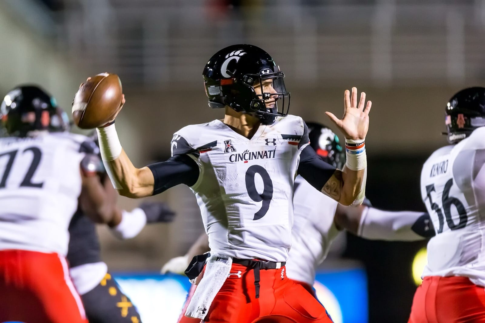Cincinnati quarterback Desmond Ridder sets to pass in a white Cincinnati jersey, red pants and black helmet