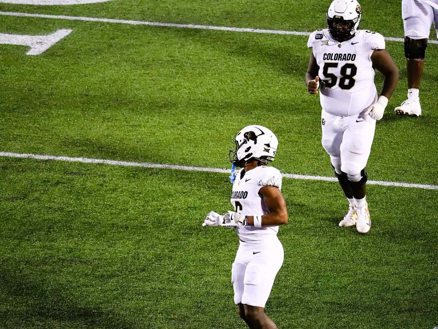 Two Colorado players in white road uniforms and white helmets with the buffalo logo at Houston
