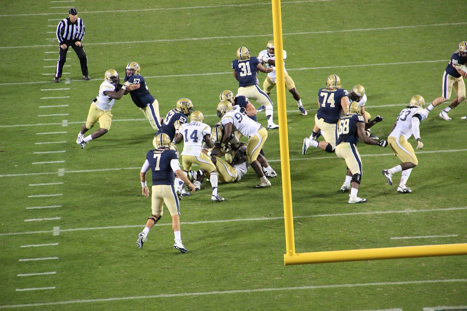 Georgia Tech defenders in white jerseys, gold pants and gold GT helmets tackle a Pitt ball carrier at Bobby Dodd Stadium