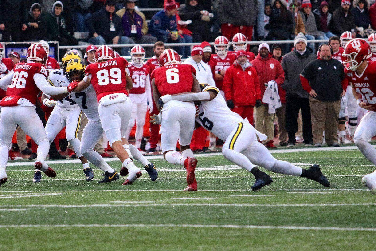 Indiana players in crimson home jerseys and white pants blocking at the line against Michigan in Bloomington