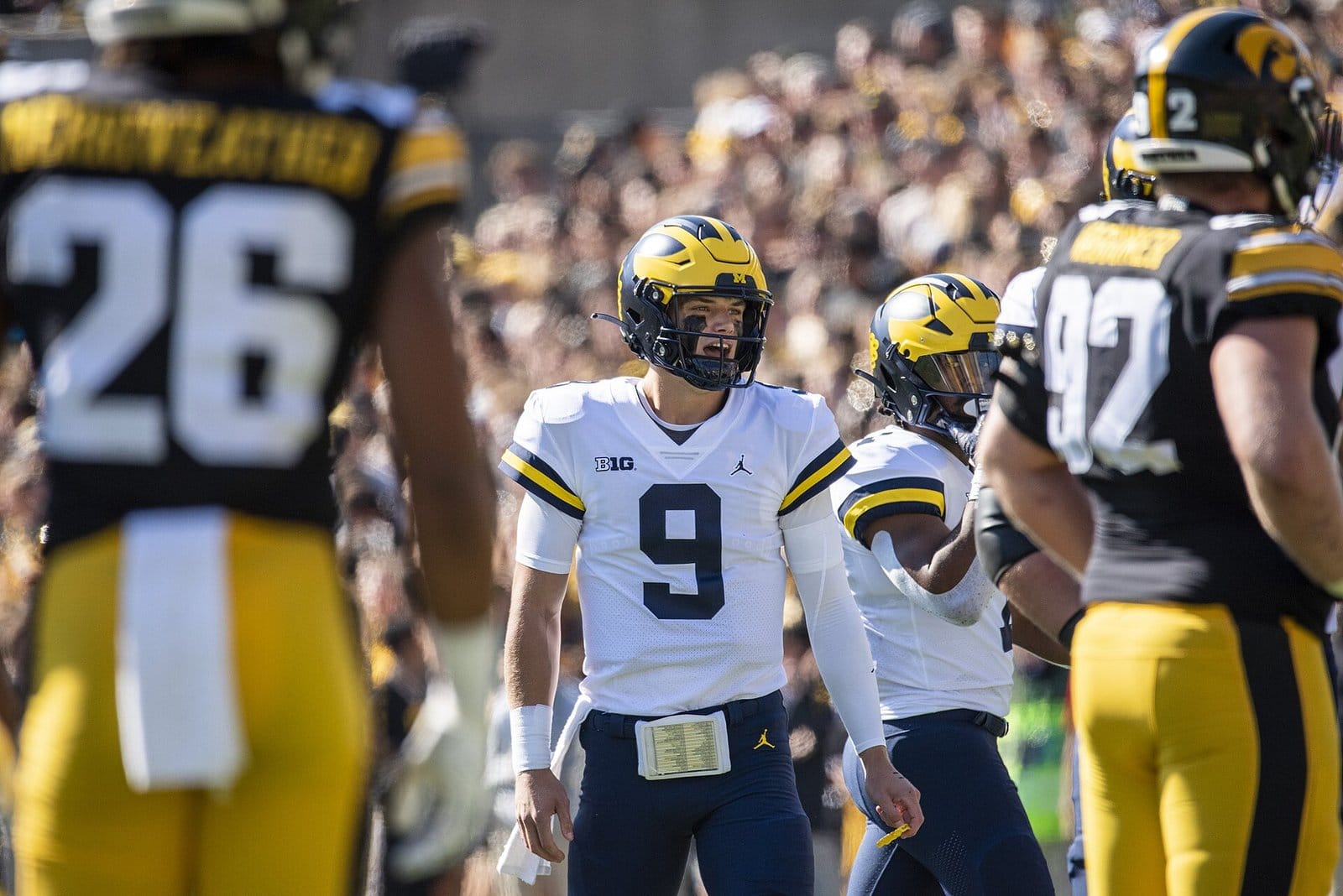 Iowa players in black home jerseys, gold pants and gold helmets around the Michigan quarterback at Kinnick Stadium