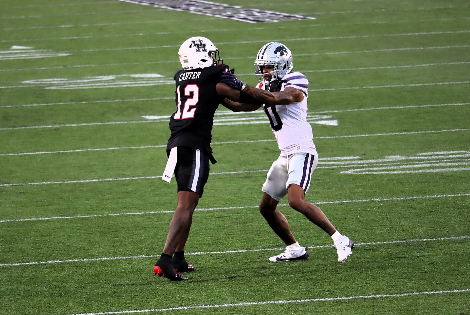 A Kansas State receiver in a white jersey and silver Powercat helmet hand-fights a Houston defender