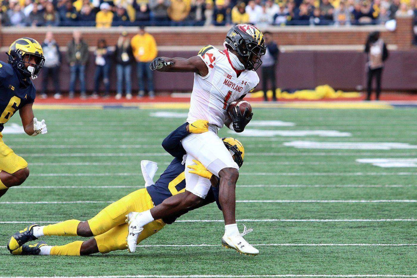 A Maryland ball carrier in the white road jersey with Maryland flag trim and black helmet breaks a tackle at Michigan Stadium