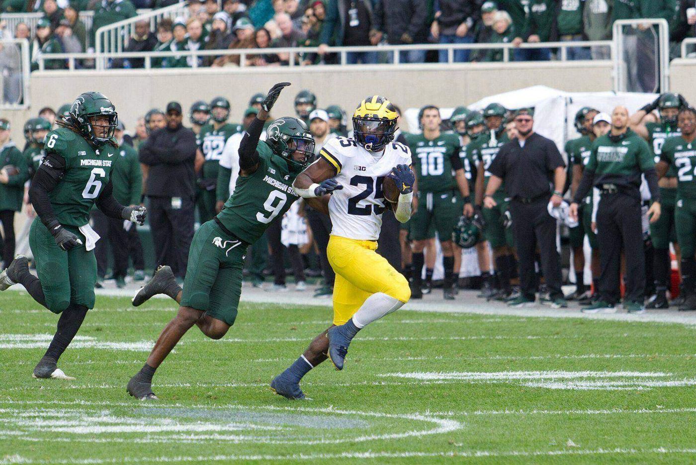 Michigan State players in green home jerseys, green pants and green helmets in pursuit at Spartan Stadium