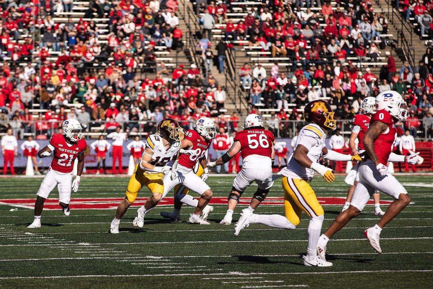 Rutgers players in scarlet home jerseys and scarlet helmets run downfield on a kick at SHI Stadium