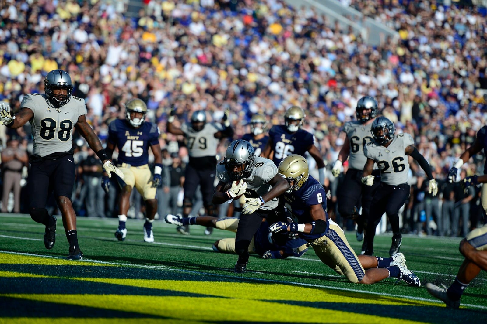UCF players in white jerseys and black helmets as a UCF runner is tackled near the goal line at Navy