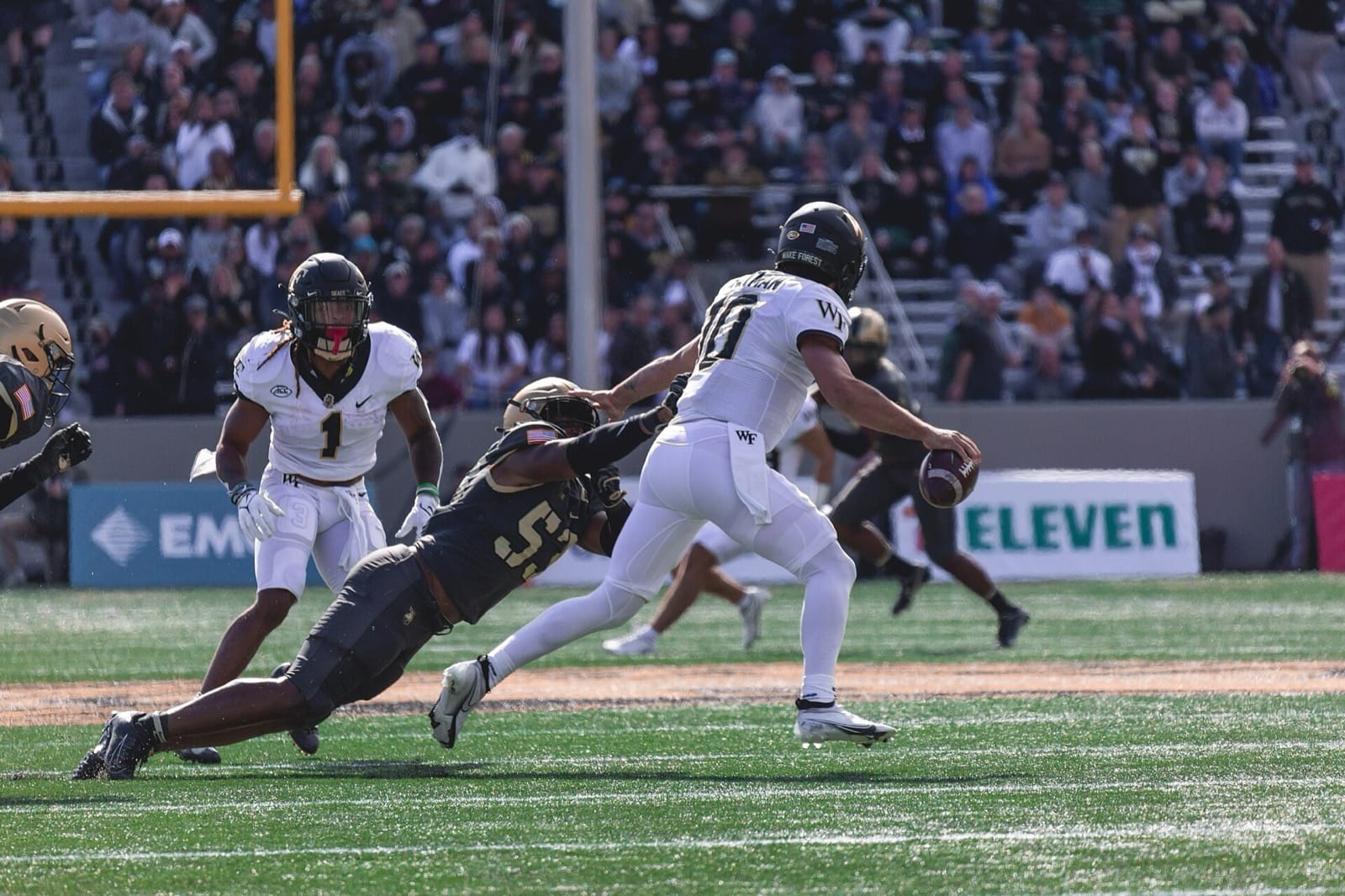 A Wake Forest quarterback in a white road jersey and black helmet throws under pressure at Army