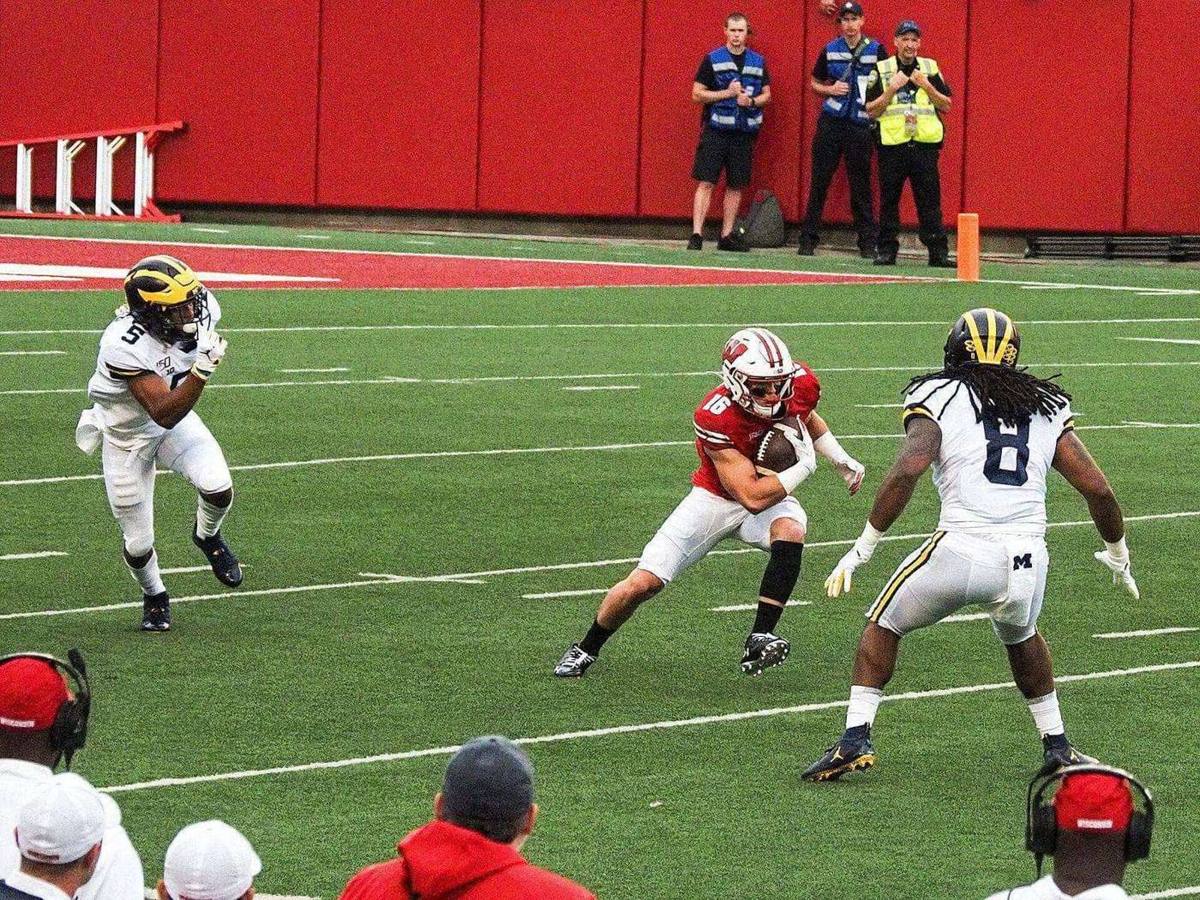 A Wisconsin ball carrier in the red home jersey and white helmet cuts between Michigan defenders at Camp Randall Stadium