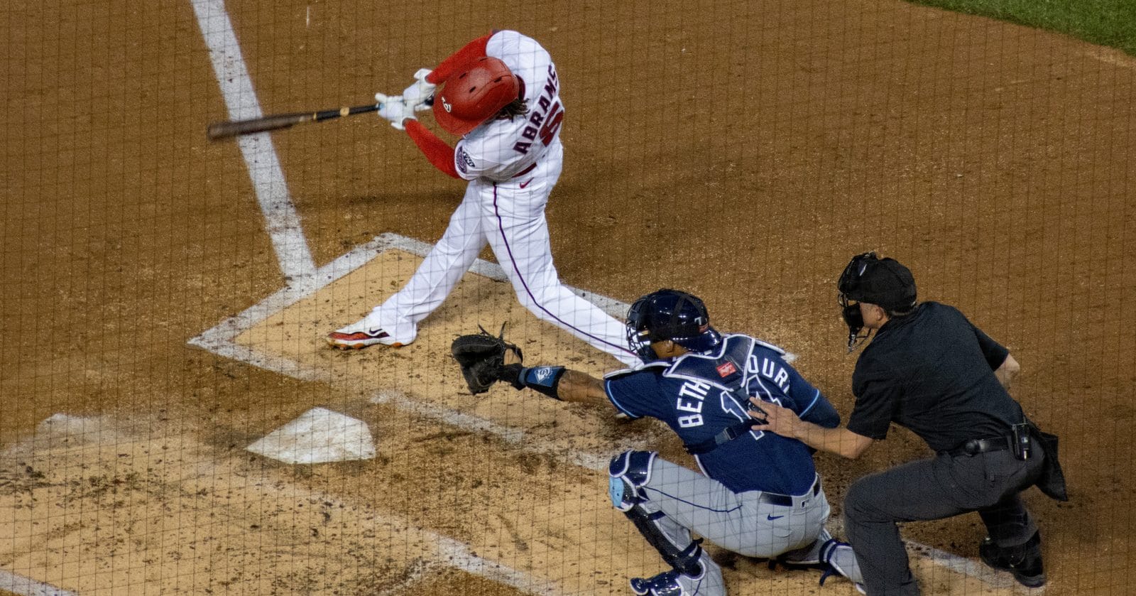 CJ Abrams swings in the Nationals' home white uniform and red helmet