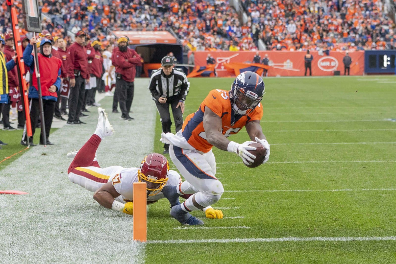 Broncos running back Melvin Gordon dives for a touchdown in the orange home jersey with navy shoulders, white pants and navy helmet, against Washington at Empower Field at Mile High in Denver on Oct. 31, 2021