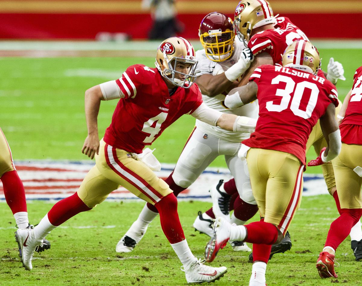San Francisco 49ers quarterback Nick Mullens hands off to Jeff Wilson Jr. in red home jerseys and gold helmets during a 2020 game