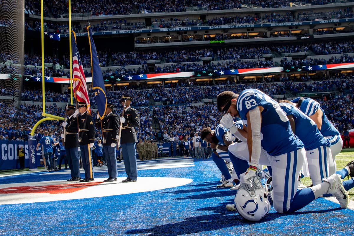 Colts players in blue home jerseys kneel in the end zone before a 2022 home game at Lucas Oil Stadium