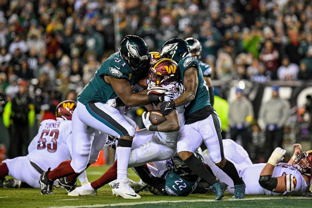 Philadelphia Eagles defenders in midnight green jerseys make a tackle against the Washington Commanders at Lincoln Financial Field in 2022