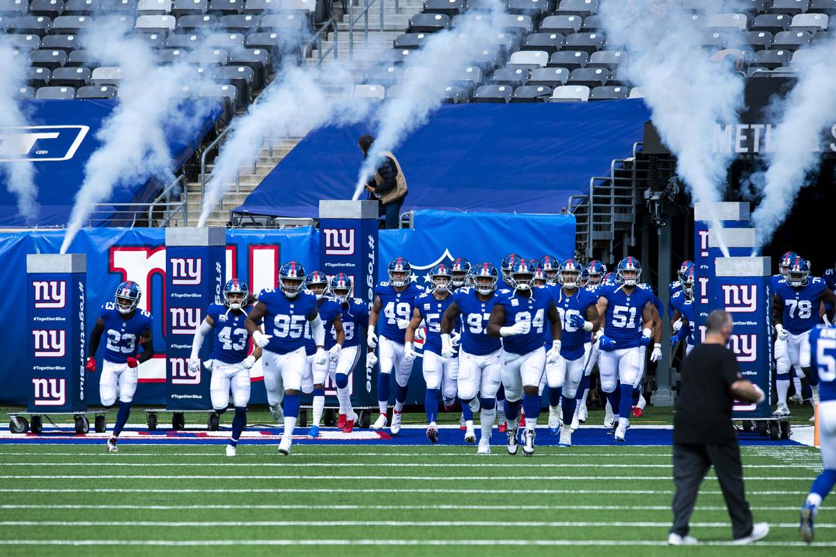 New York Giants players in royal blue jerseys run onto the field through smoke at MetLife Stadium in 2020