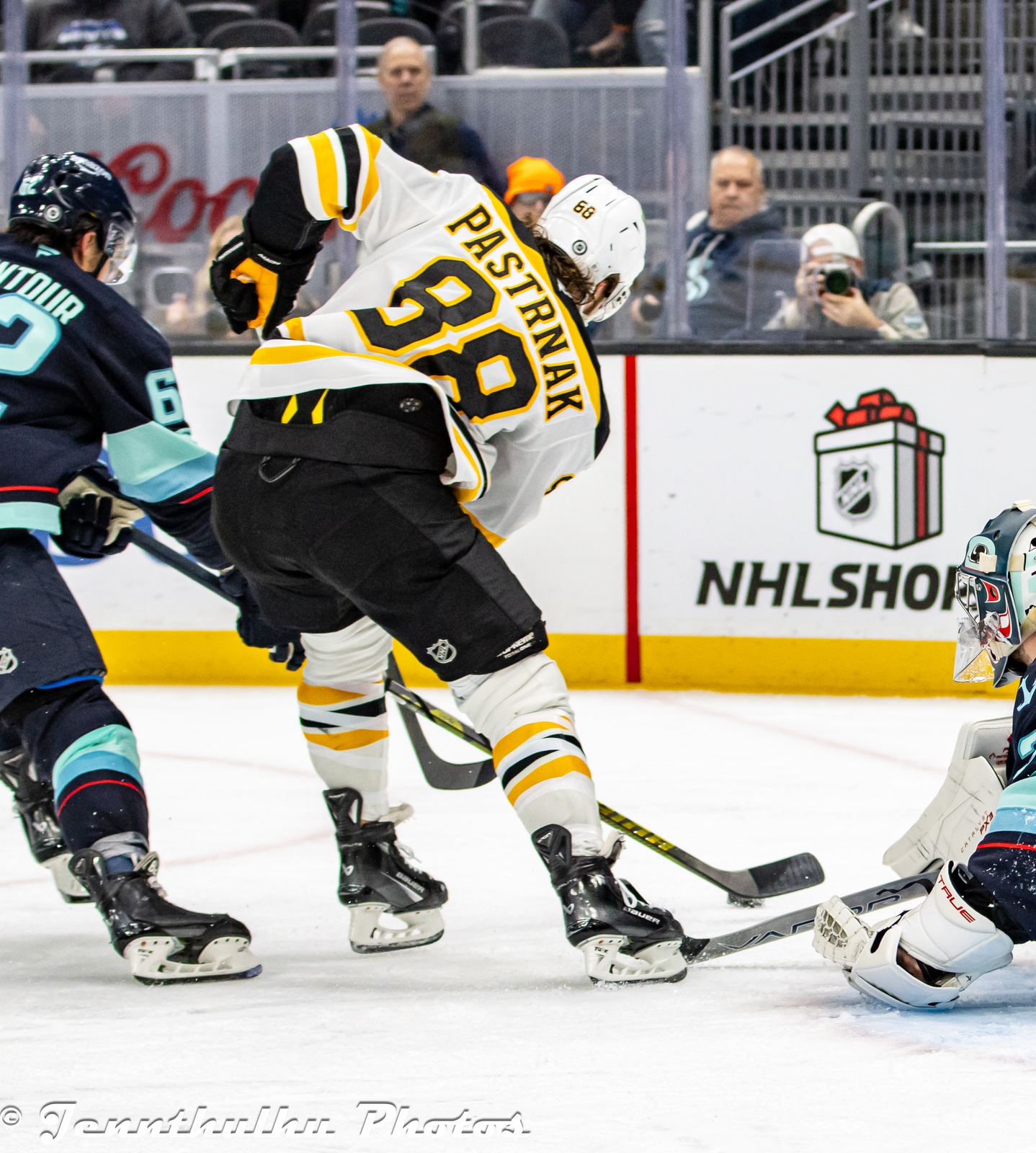 David Pastrnak drives to the net in the Bruins' white road uniform, spoked-B crest and PASTRNAK over No. 88, against Kraken goalie Philipp Grubauer at Climate Pledge Arena in Seattle, December 12, 2024