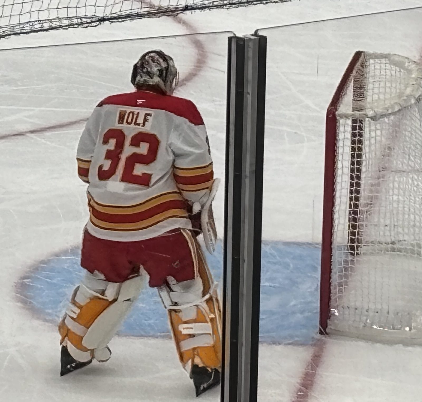 Goalie Dustin Wolf, seen from behind in the Flames' white road uniform with red and gold stripes and WOLF over No. 32, at a preseason game at Climate Pledge Arena in Seattle, October 4, 2026