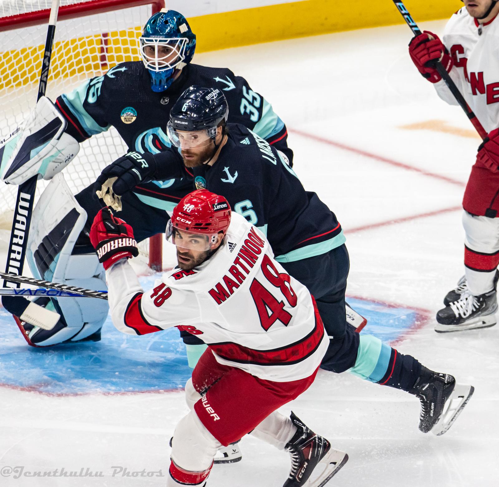 Jordan Martinook in the Hurricanes' white road uniform with red trim, MARTINOOK over No. 48, battles in front of the Kraken net at Climate Pledge Arena in Seattle, October 19, 2023