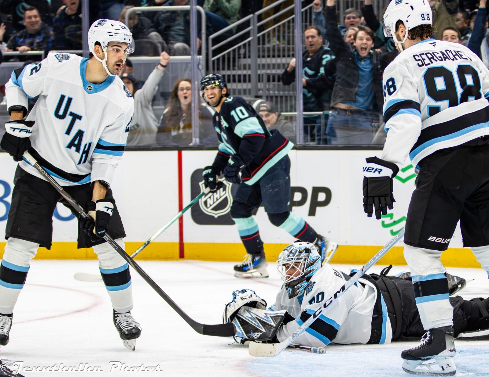 Mikhail Sergachev (No. 98) and teammates in Utah Hockey Club's 2024-25 white road uniform with the diagonal UTAH wordmark as goalie Karel Vejmelka lies in the crease at Climate Pledge Arena in Seattle, December 30, 2024