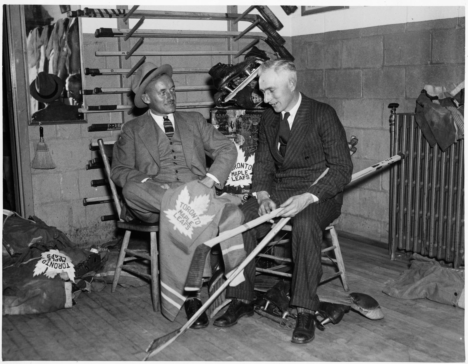 Conn Smythe, who renamed the Toronto St. Patricks the Maple Leafs in 1927, sits with coach Dick Irvin holding a Maple Leafs blanket and sticks, around 1931-32