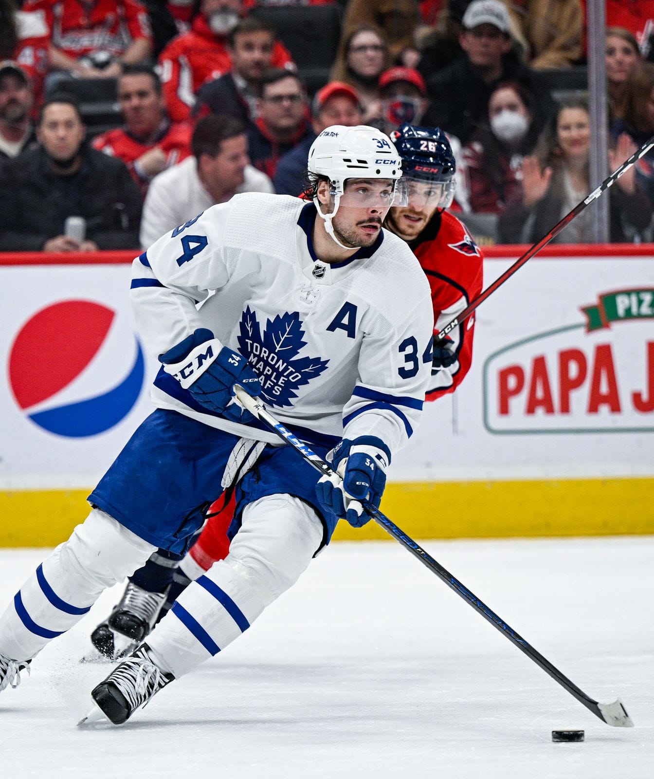Auston Matthews carries the puck in the Maple Leafs' white road uniform with the blue maple leaf crest and an A, No. 34, at Capital One Arena in Washington, February 28, 2022