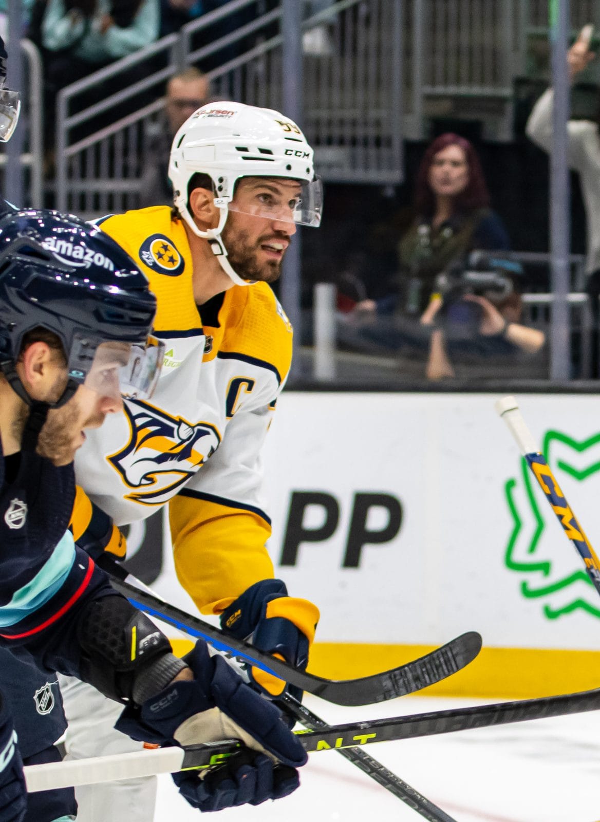 Captain Roman Josi in the Predators' white road uniform with gold shoulders and the saber-toothed cat crest battles the Kraken's Alexander Wennberg and Jordan Eberle at Climate Pledge Arena in Seattle, November 2023