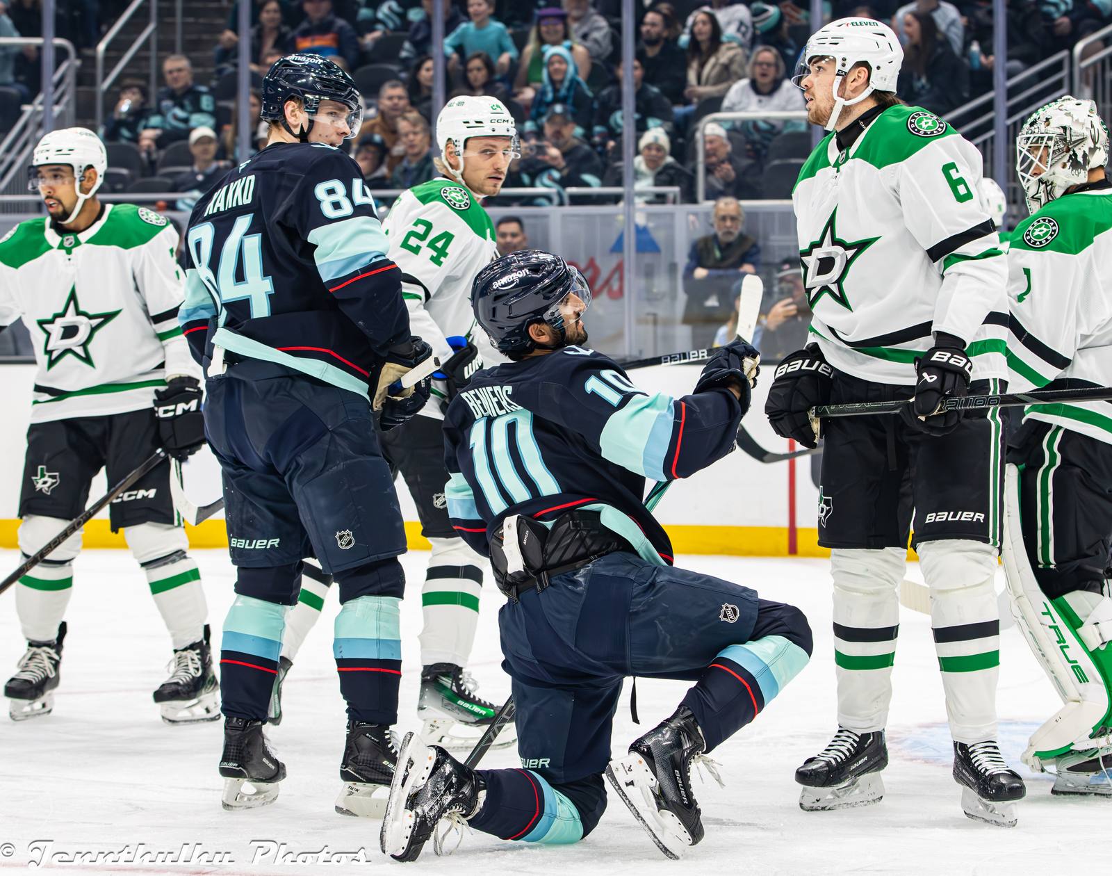 Stars players in white road uniforms with the green star crest, Roope Hintz (No. 24) among them, surround a Kraken player at Climate Pledge Arena in Seattle, March 31, 2025
