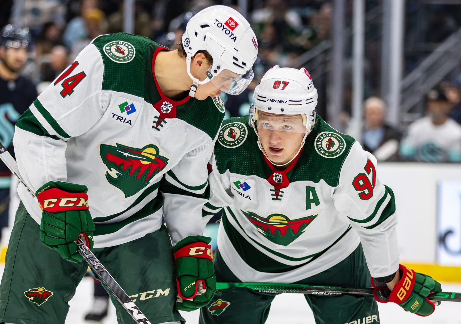 Joel Eriksson Ek (No. 14) and Kirill Kaprizov (No. 97, with an A) in the Wild's white road uniforms with the Wild crest and green and red trim at Climate Pledge Arena in Seattle, December 10, 2023
