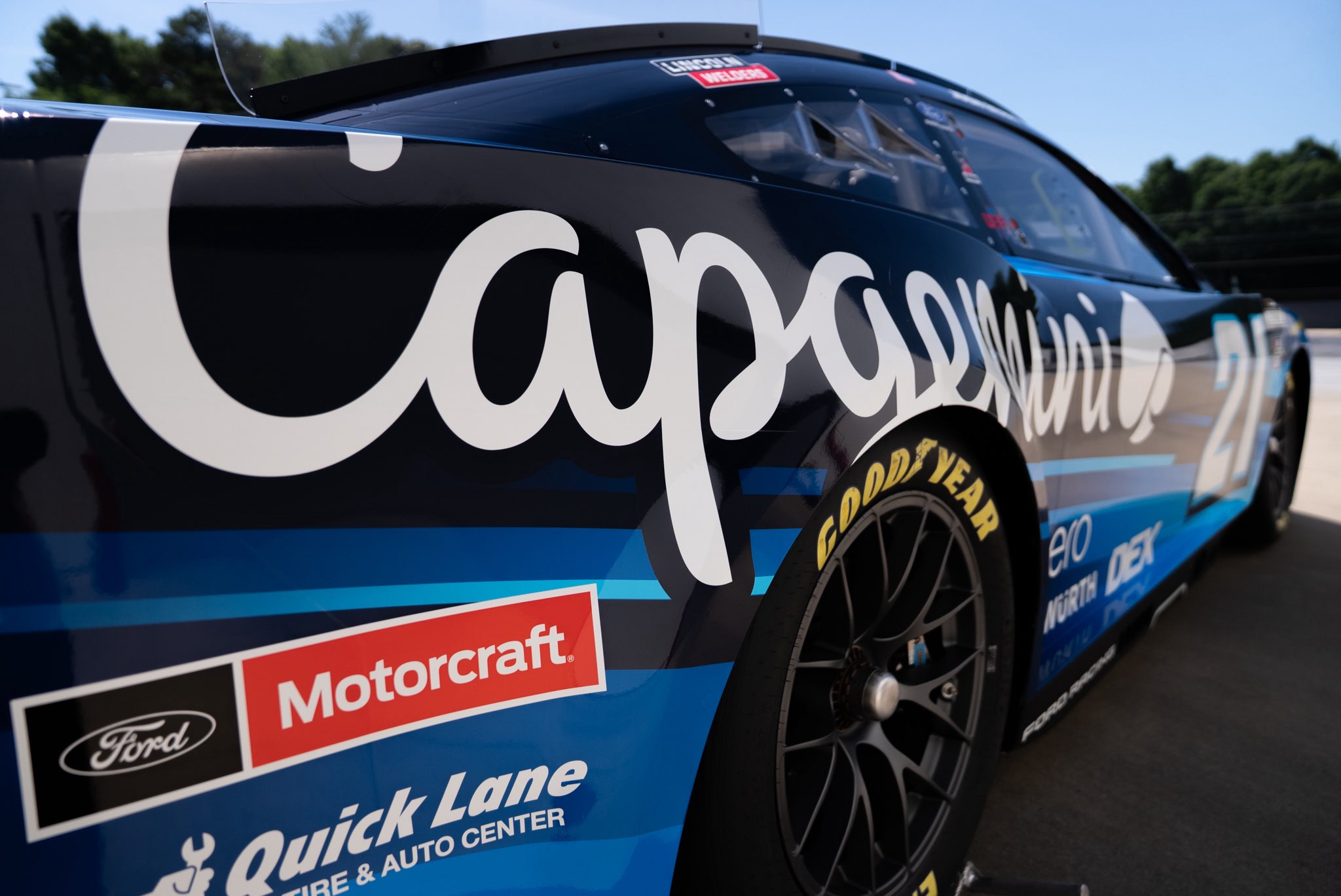 Close-up of the Capgemini script wordmark on the side of Josh Berry's #21 Wood Brothers Racing Ford Mustang Dark Horse paint scheme for the 2026 NASCAR Cup Series with the Motorcraft Quick Lane Tire and Auto Center sponsor lockup on the lower quarter panel