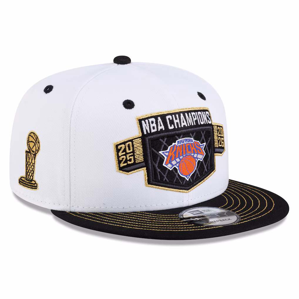 New York Knicks 2026 NBA Champions locker room New Era 9FIFTY snapback hat in white with a black brim, a gold-trimmed NBA Champions 2026 shield badge with the Knicks roundel on the front, a gold Larry O'Brien Trophy embroidered on the left side, and gold New Era branding
